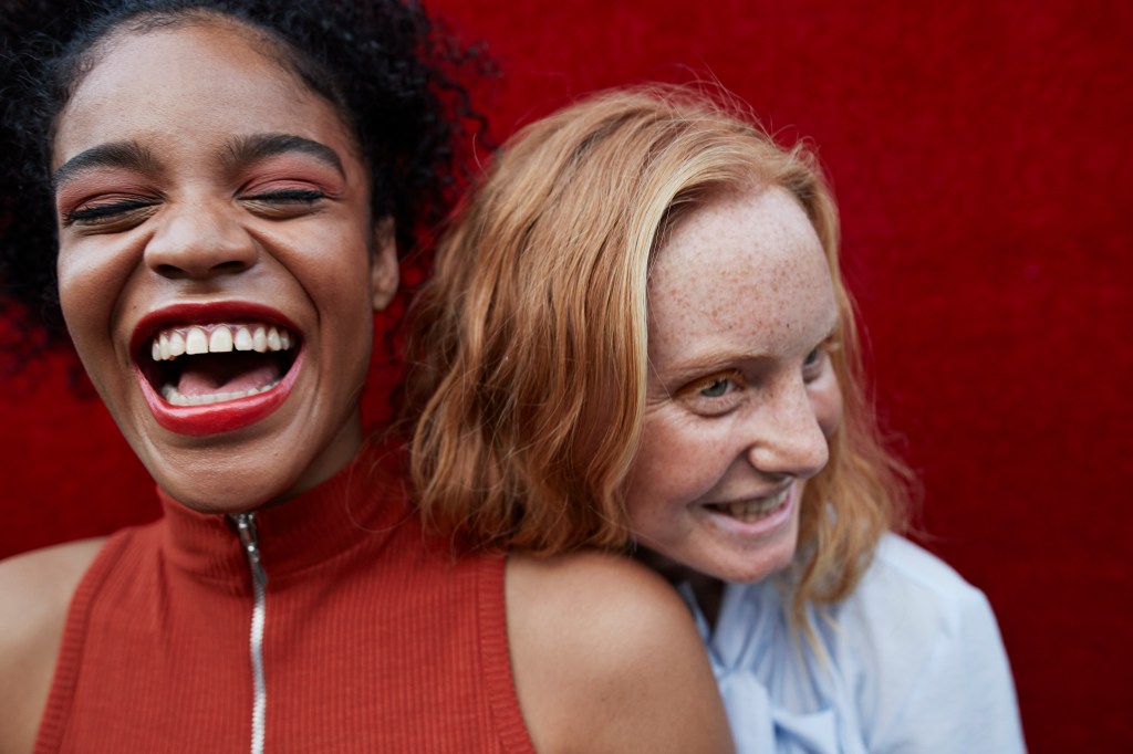 Duas mulheres jovens rindo contra uma parede vermelha