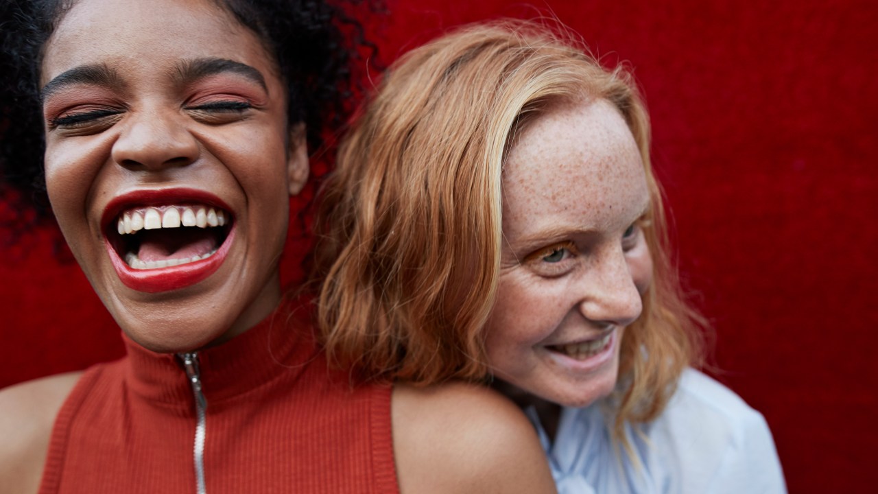Duas mulheres jovens rindo contra uma parede vermelha