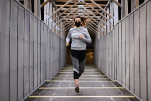 Woman doing running exercise wearing face mask and grey jumper