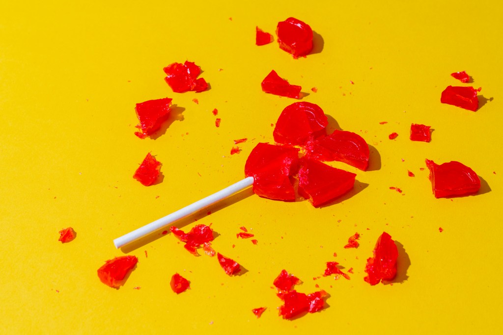 Pirulito vermelho em formato de coração partido sobre fundo amarelo