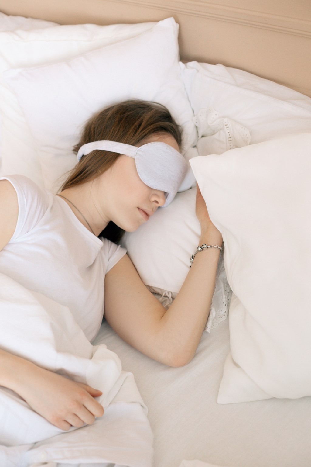 mulher dormindo sobre cama branca e tapa olhos branco.