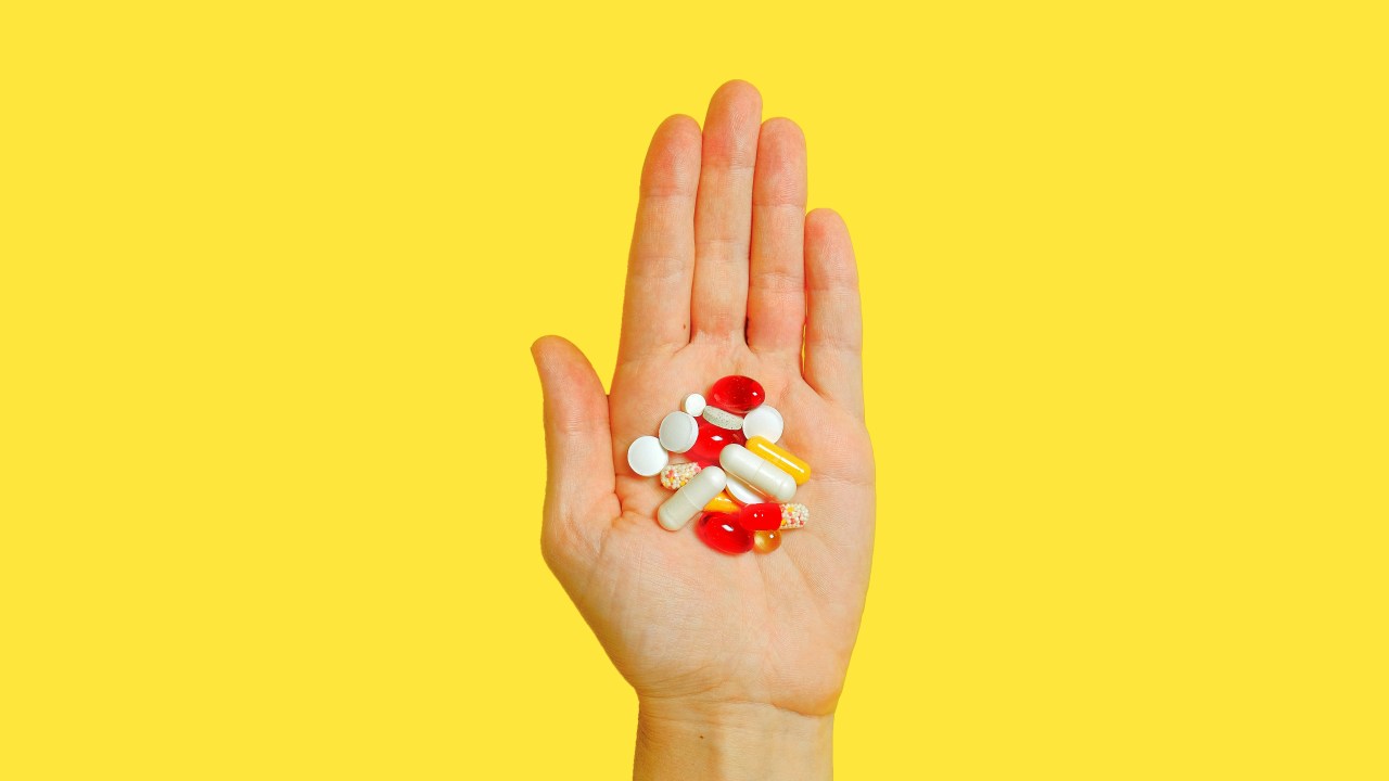 mão segurando diversas pílulas sobre fundo amarelo