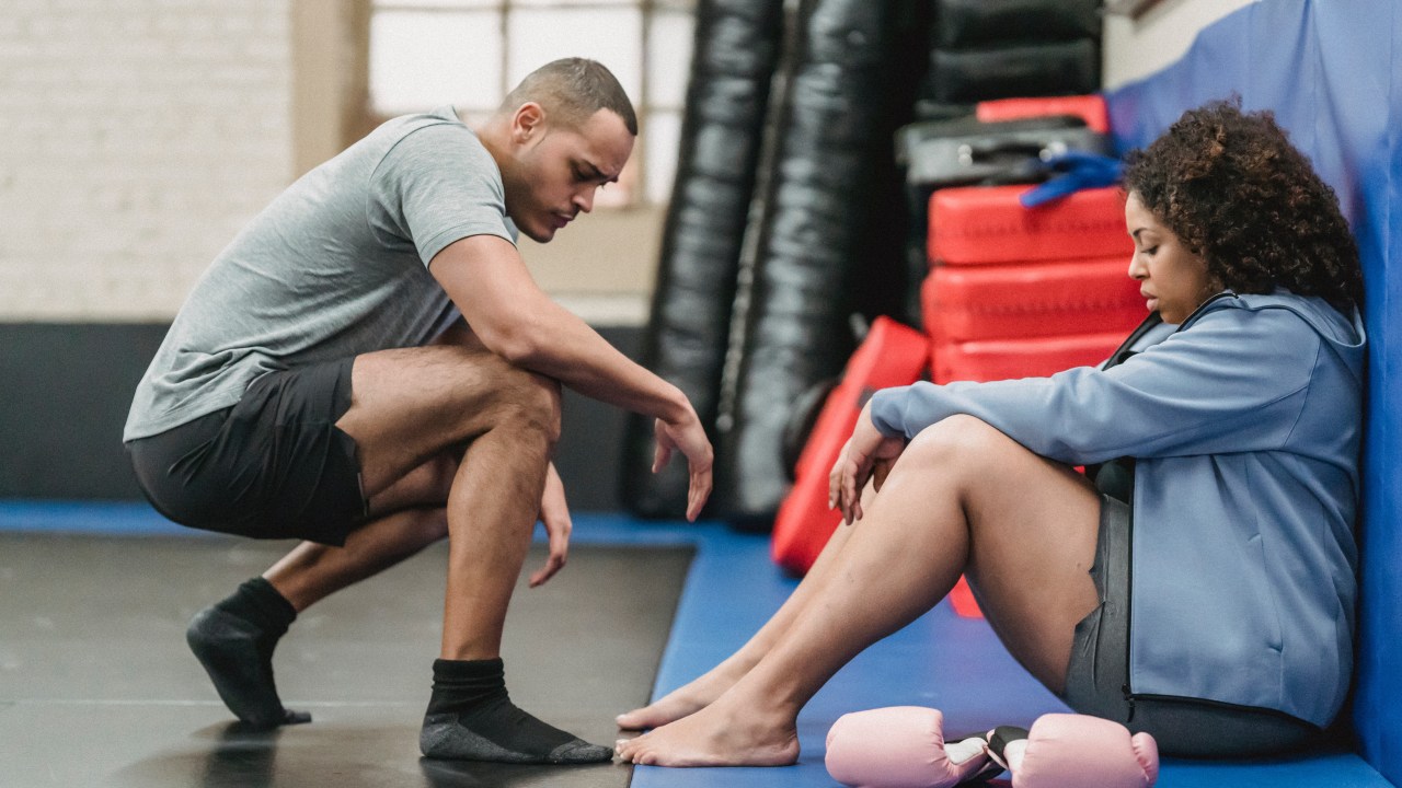 homem se abaixando para ajudar a companheira de treino em academia de boxe