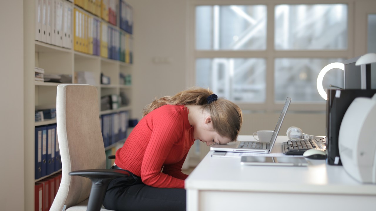 mulher cansada, deitada sobre o computador em ambiente de trabalho