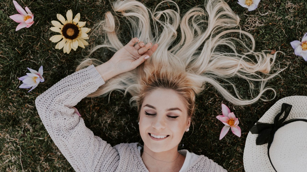 mulher deitada com sorriso no rosto e flores espalhadas ao redor