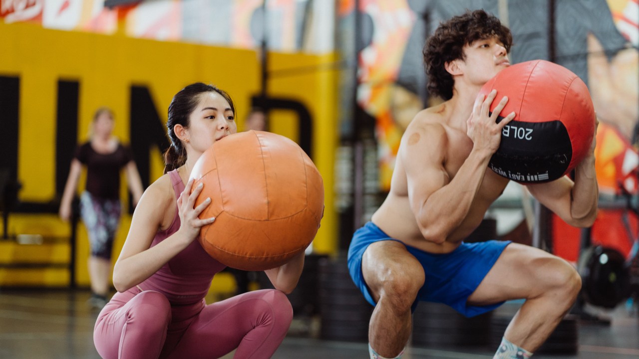 homem e mulher na academia, fazendo agachamento com bola de peso