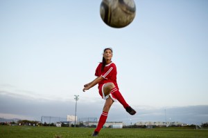 Female soccer player kicking the ball over camera