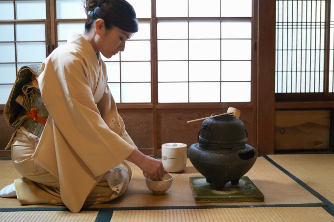 Japan, Tokyo, woman kneeling on floor, preparing tea, side view