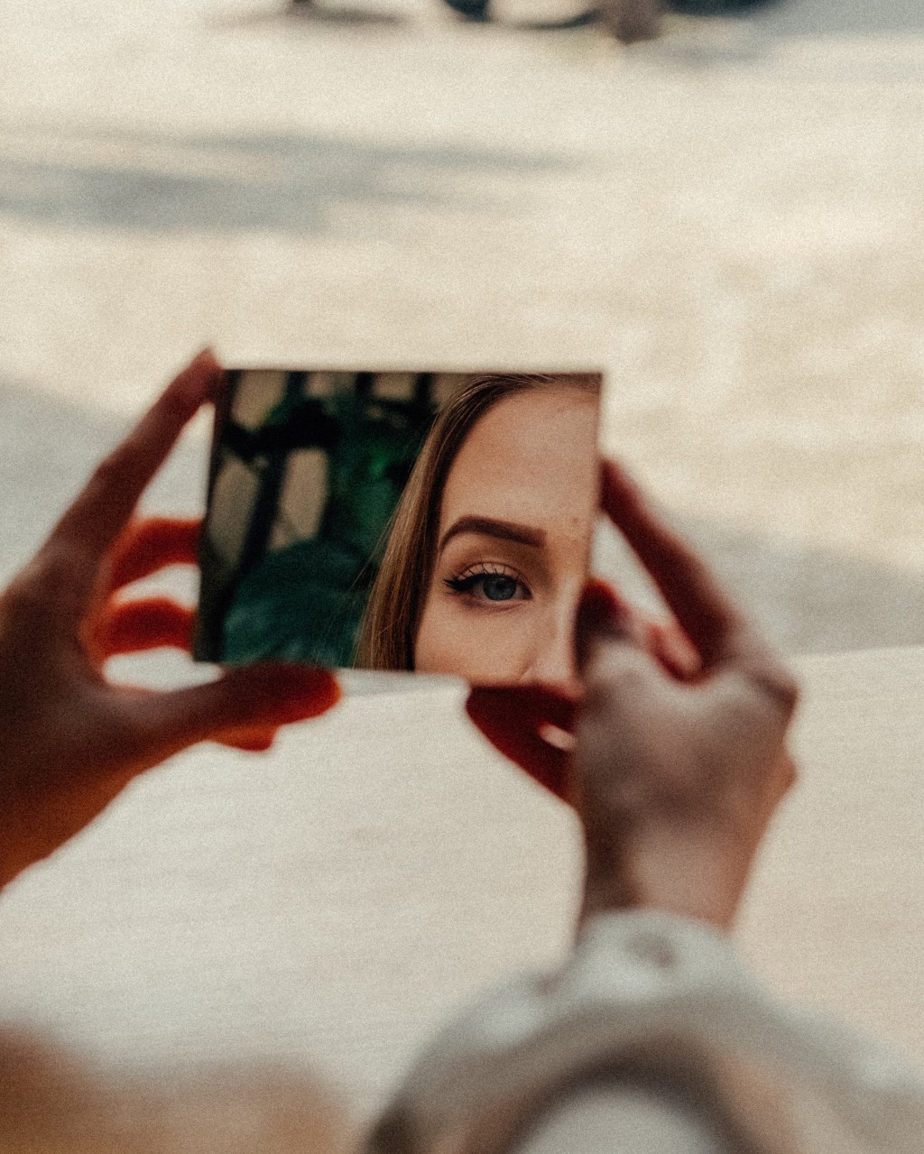 mulher olhando parte de seu reflexo (olho e sobrancelha) por espelho de mão