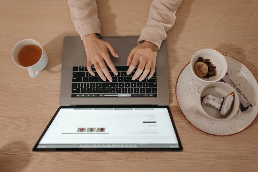 mão de uma mulher sobre teclado do computador com bolachas e café em volta.
