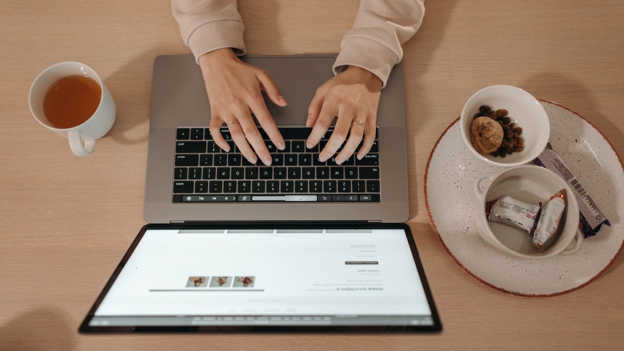 mão de uma mulher sobre teclado do computador com bolachas e café em volta.