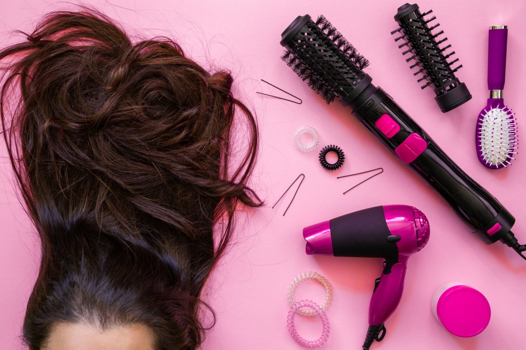 cabelo de mulher sobre fundo rosa ao lado escovas, secadores e escovas secadoras