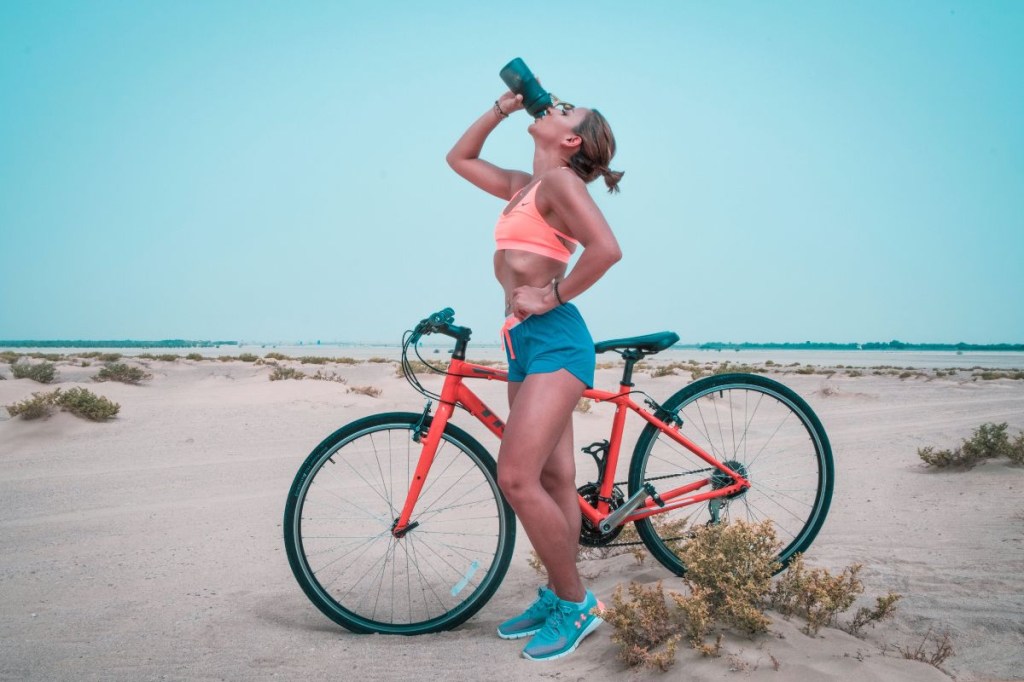 Mulher bebendo água com bicicleta ao lado