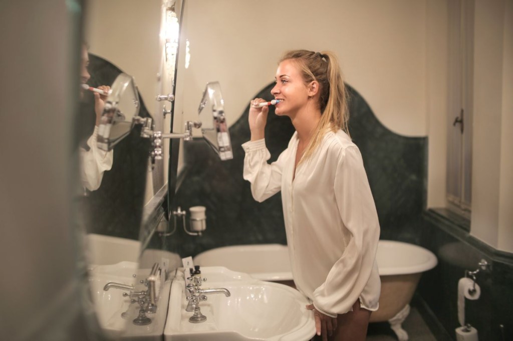 Mulher escovando os dentes se olhando no espelho
