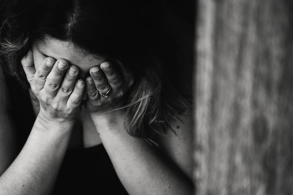 Foto em preto e branco de uma mulher chorando com as mãos no rosto