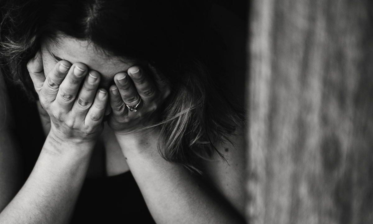 Foto em preto e branco de uma mulher chorando com as mãos no rosto