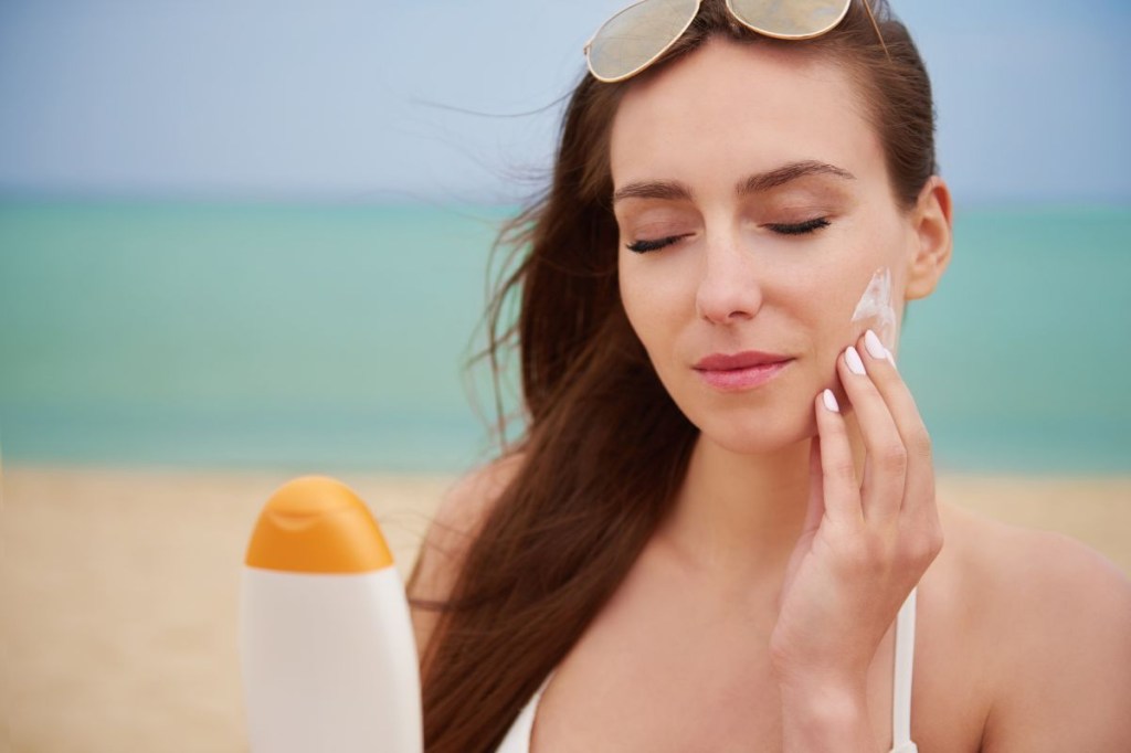 Mulher passando protetor solar no rosto na praia
