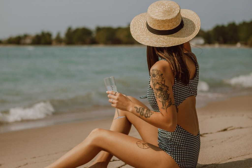 Mulher de chapéu e tatuagem na praia