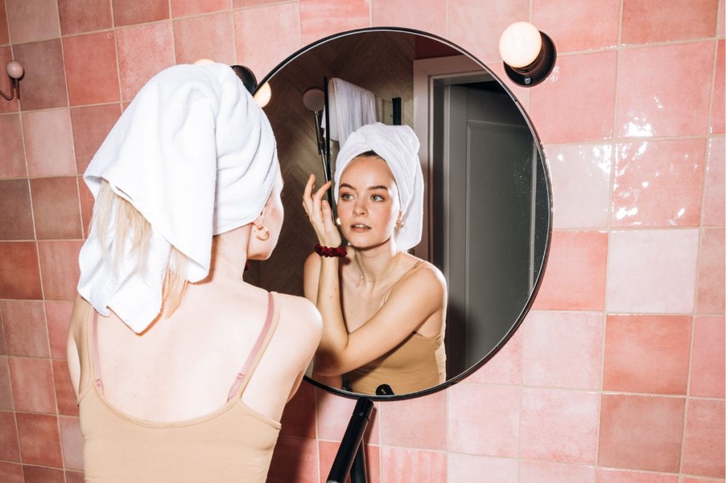 Mulher com toalha na cabeça se olhando no espelho