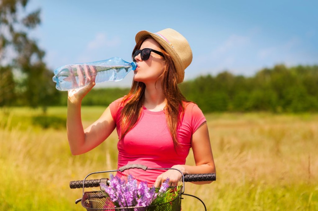 Mulher com bicicleta bebendo água durante dia quente