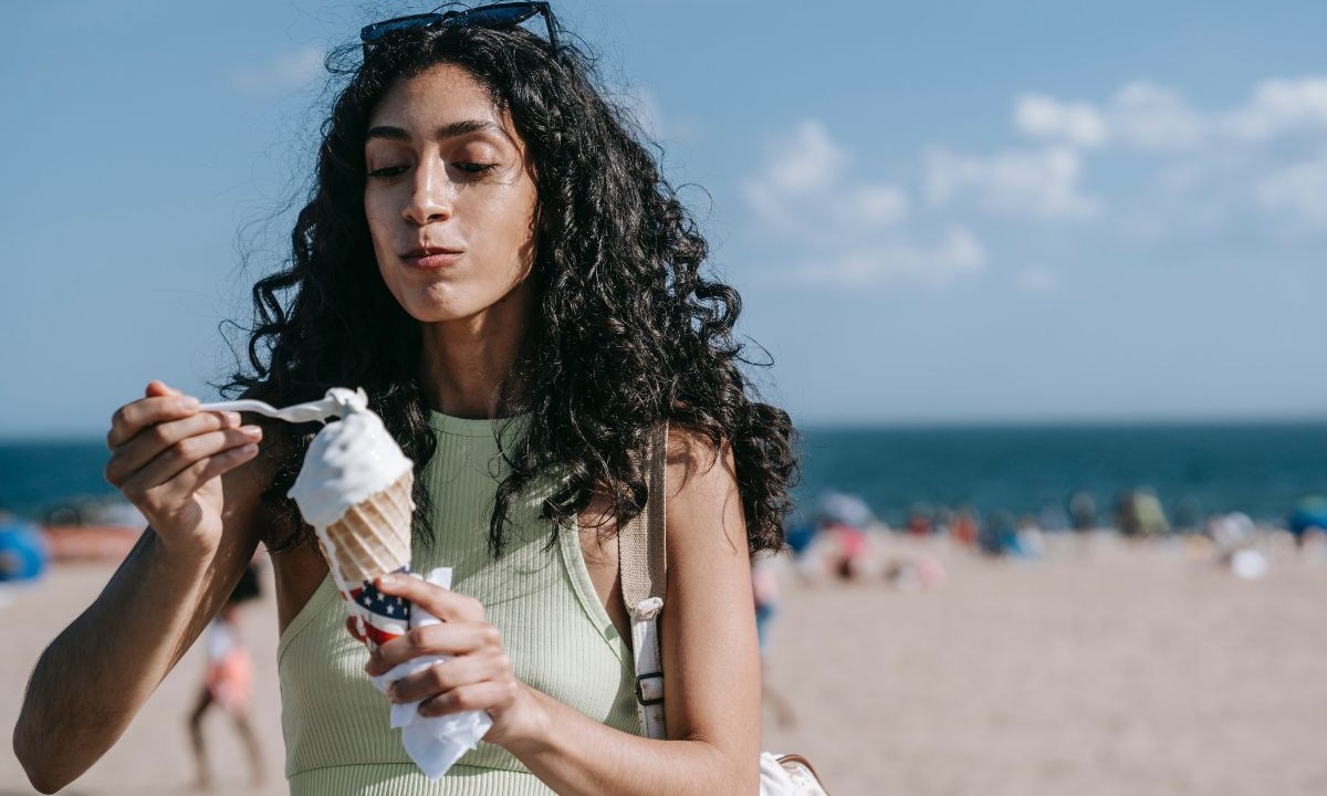 Mulher de cabelos cacheados tomando sorvete na praia