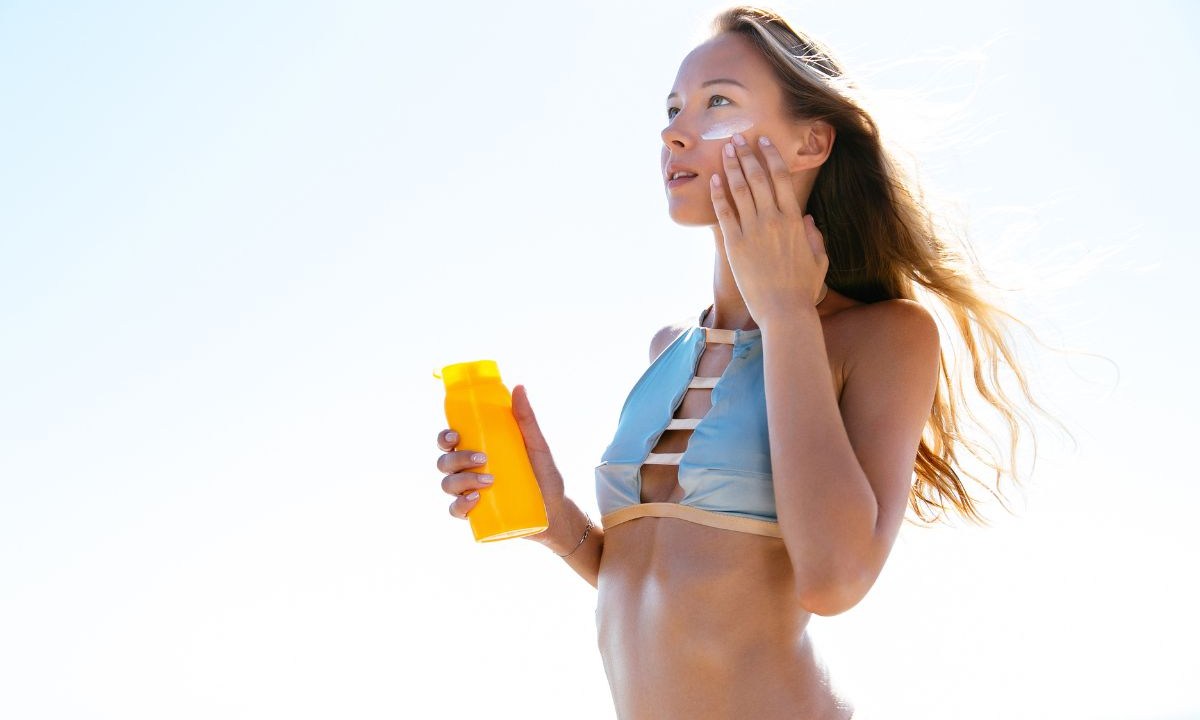 Mulher na praia aplicando protetor solar no rosto