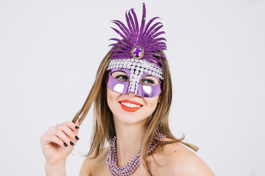 Mulher com máscara de carnaval segurando uma mecha do seu cabelo