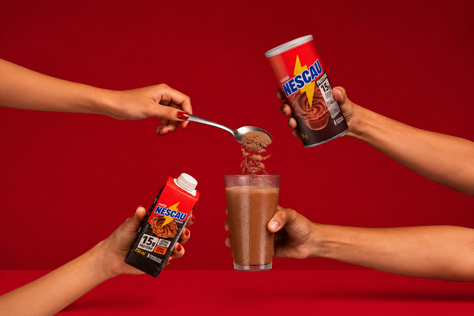 Três mãos em um fundo vermelho. Uma mão feminina com unhas vermelhas despeja Nescau em pó de uma colher para um copo de achocolatado. Outra mão feminina segura uma embalagem de Nescau pronto para beber. Uma mão masculina segura uma lata de Nescau em pó