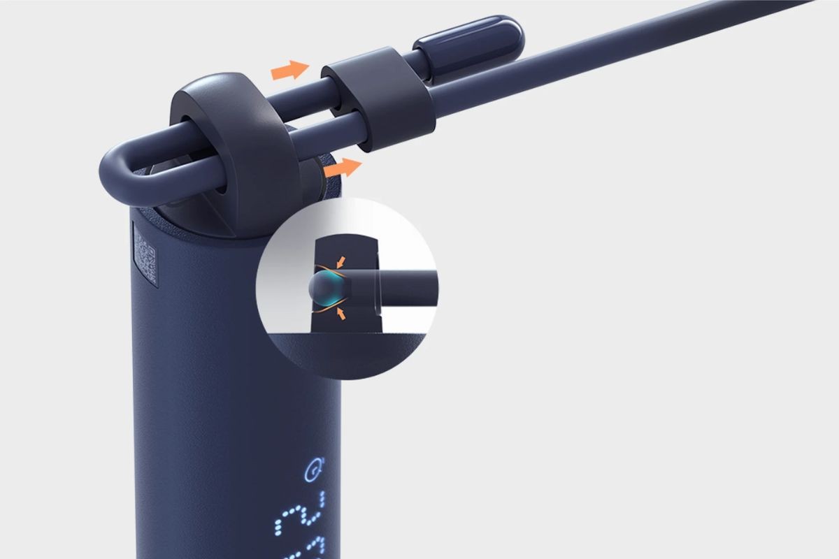 Detalhe de um dispositivo azul-marinho com um cabo flexível preso por um anel. Setas laranja indicam o movimento do cabo. Um círculo ampliado mostra o mecanismo de encaixe do cabo, com uma esfera azul pressionada entre duas superfícies, também com setas laranja indicando a pressão. Na parte inferior do dispositivo, números digitais 22 e um ícone de bateria são visíveis