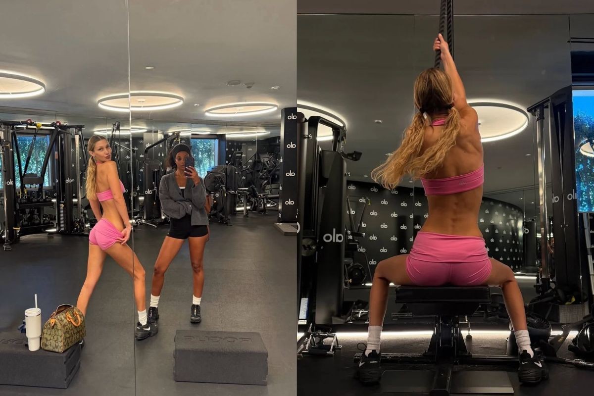 Duas mulheres em uma academia moderna. À esquerda, uma mulher loira de top e shorts rosa posa para a câmera, enquanto uma mulher negra de shorts e casaco cinza tira uma selfie no espelho. À direita, a mulher loira de costas, com tranças, sobe uma corda, exibindo músculos das costas